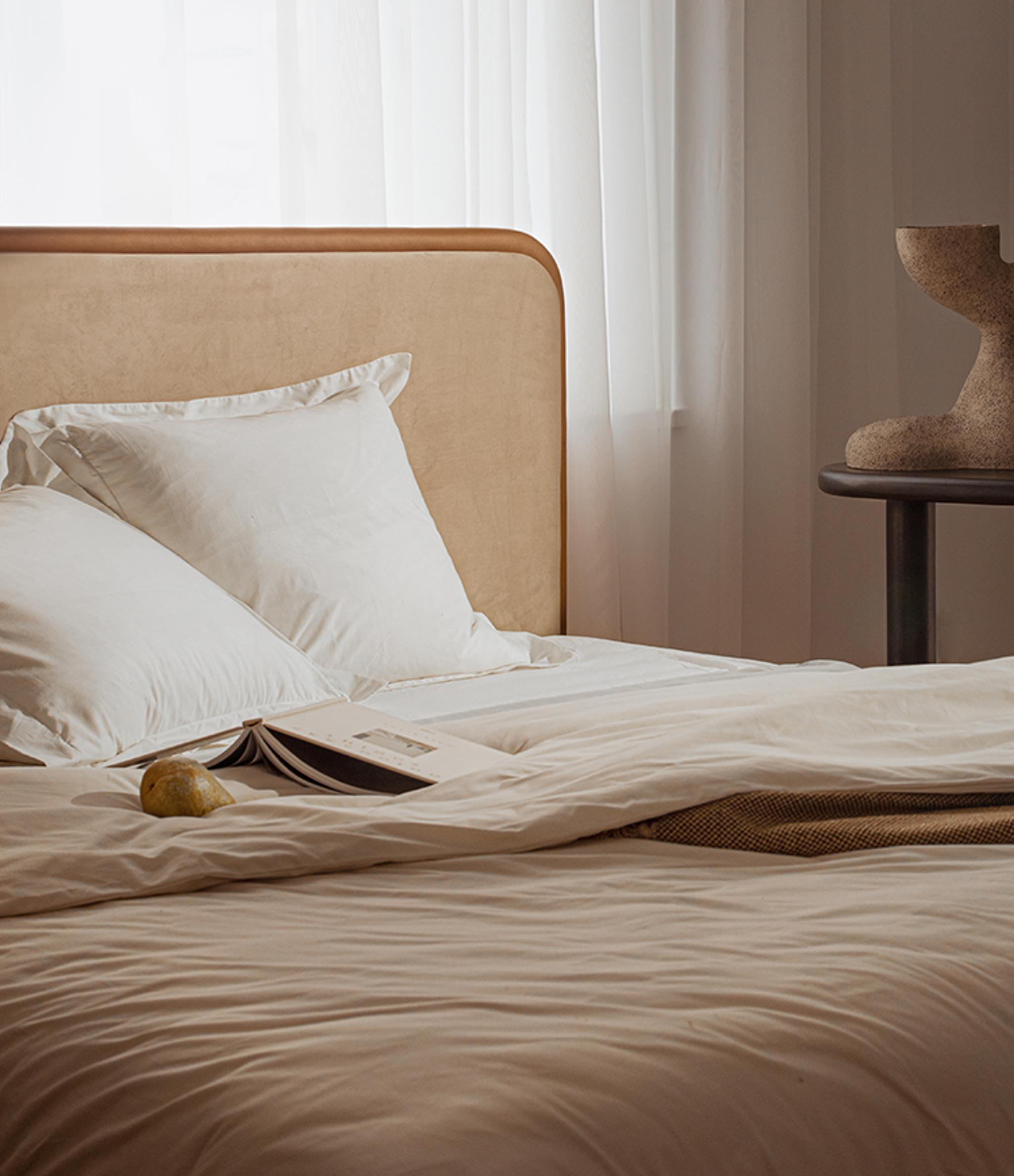 Lit Micadoni avec tête de lit capitonnée et encadrement en bois arrondi, linge de lit blanc, lumière douce.