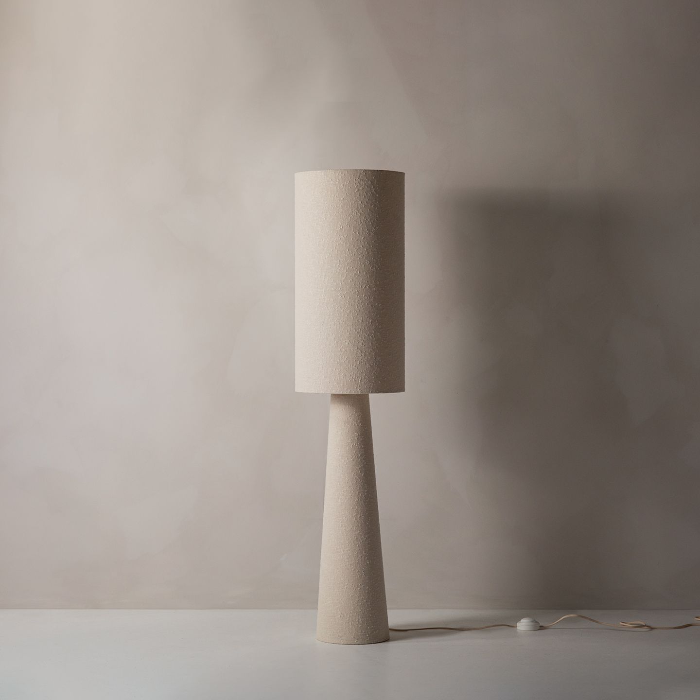 Lampe de table Micadoni beige texturé, abat-jour cylindrique sur pied conique, vue studio.