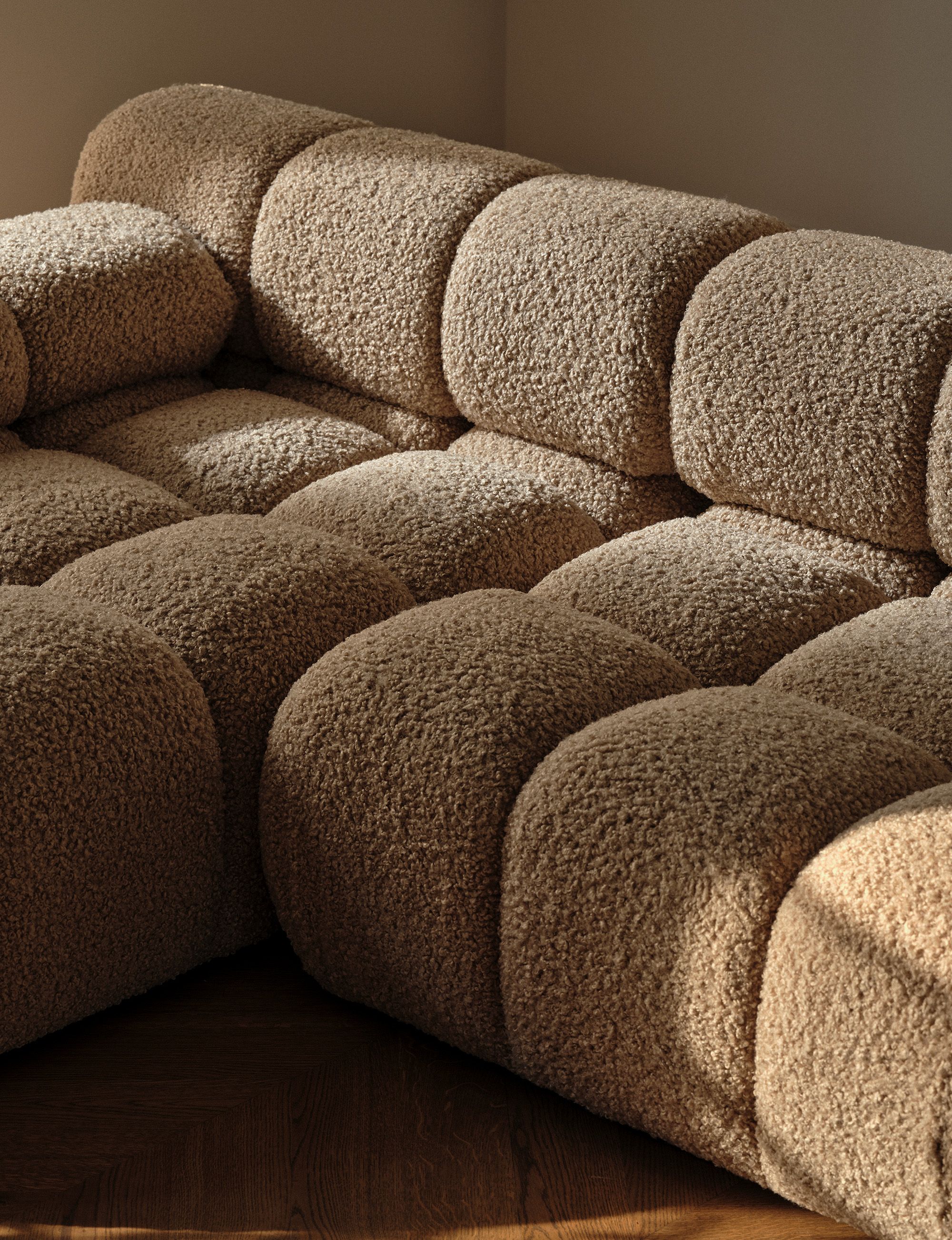 Nahaufnahme des modularen Ecksofas Micadoni Lupine in beigem Stoff mit abgerundeter Kanalkapitonierung, mit Ball-Kissen und braunem Kissen.