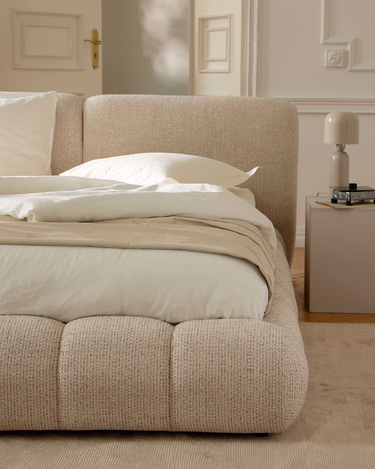 Micadoni Solange bed in textured bouclé with rounded headboard and padded base, styled in a calm beige bedroom.