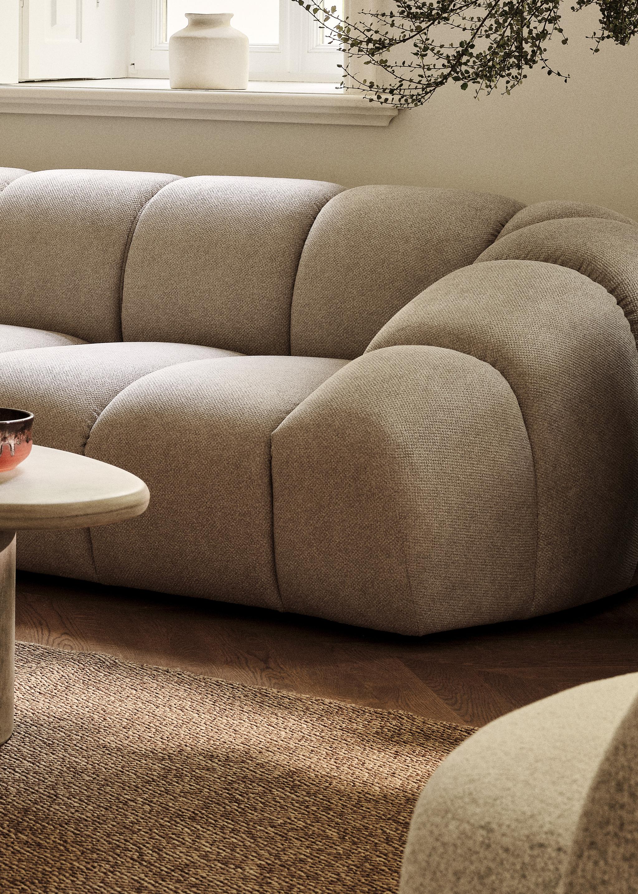 Canapé Diana en tissu structuré beige aux lignes arrondies, associé à la table basse sculpturale Daria en pierre – mobilier Micadoni