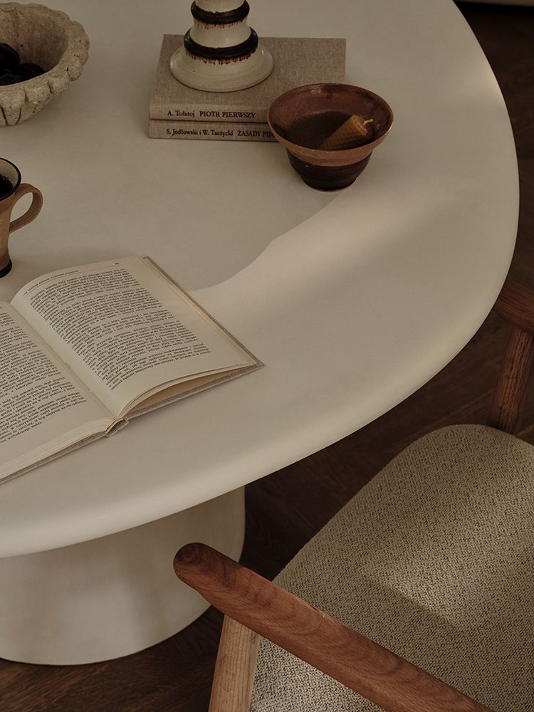 Table de salle à manger Micadoni Daria dans une ambiance chaleureuse, avec céramiques, livre ouvert et fauteuil texturé.