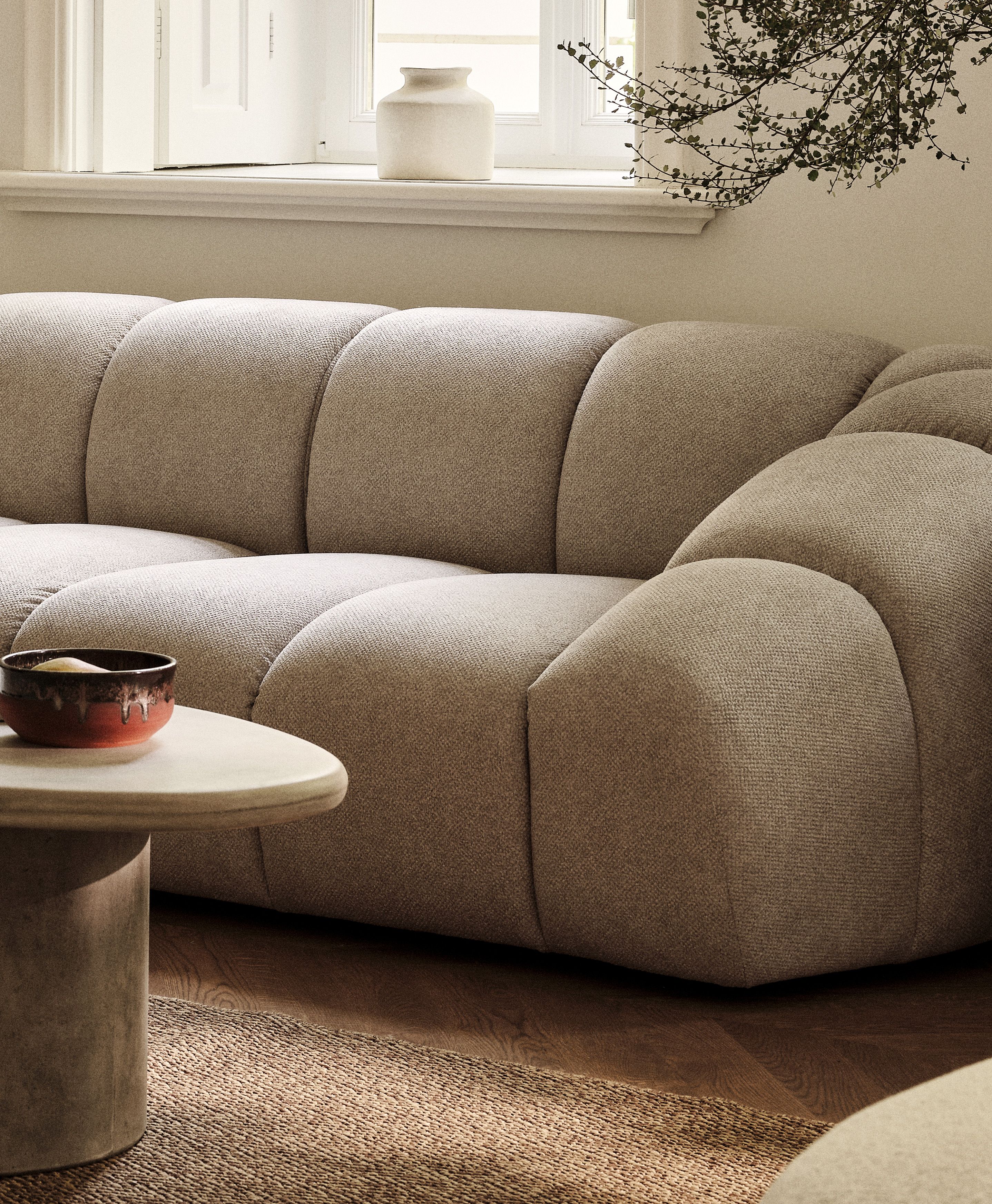 Canapé Diana en tissu structuré beige aux lignes arrondies, associé à la table basse sculpturale Daria en pierre – mobilier Micadoni